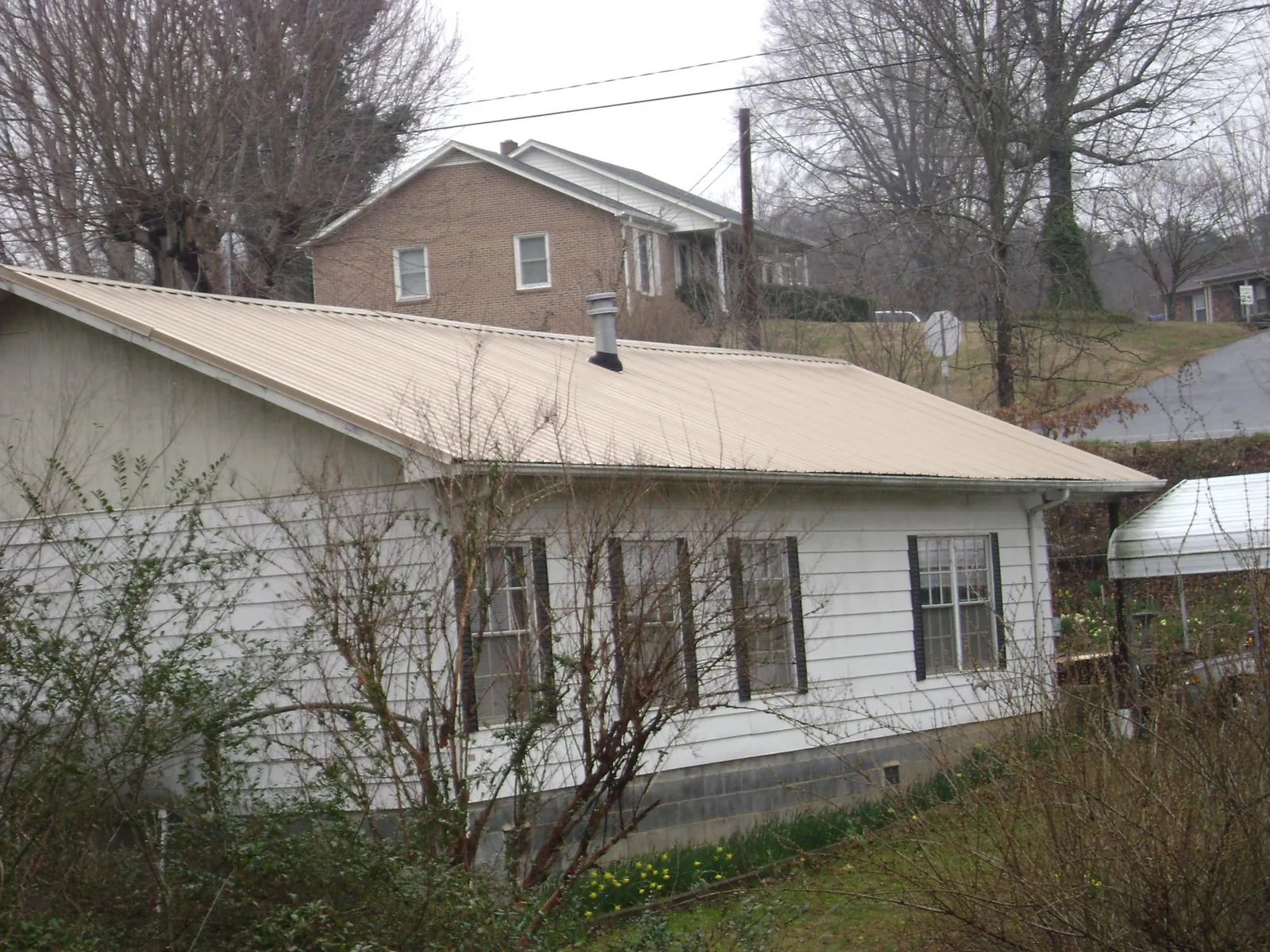 Tan metal roof on a white sided house set into a hillside — Commercial Roofing by Roofing Brothers in Florence